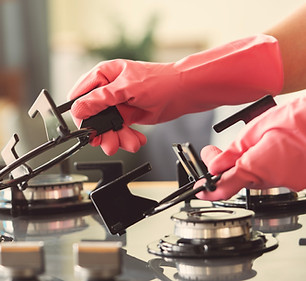 Gloved hands deep cleaning a gas range